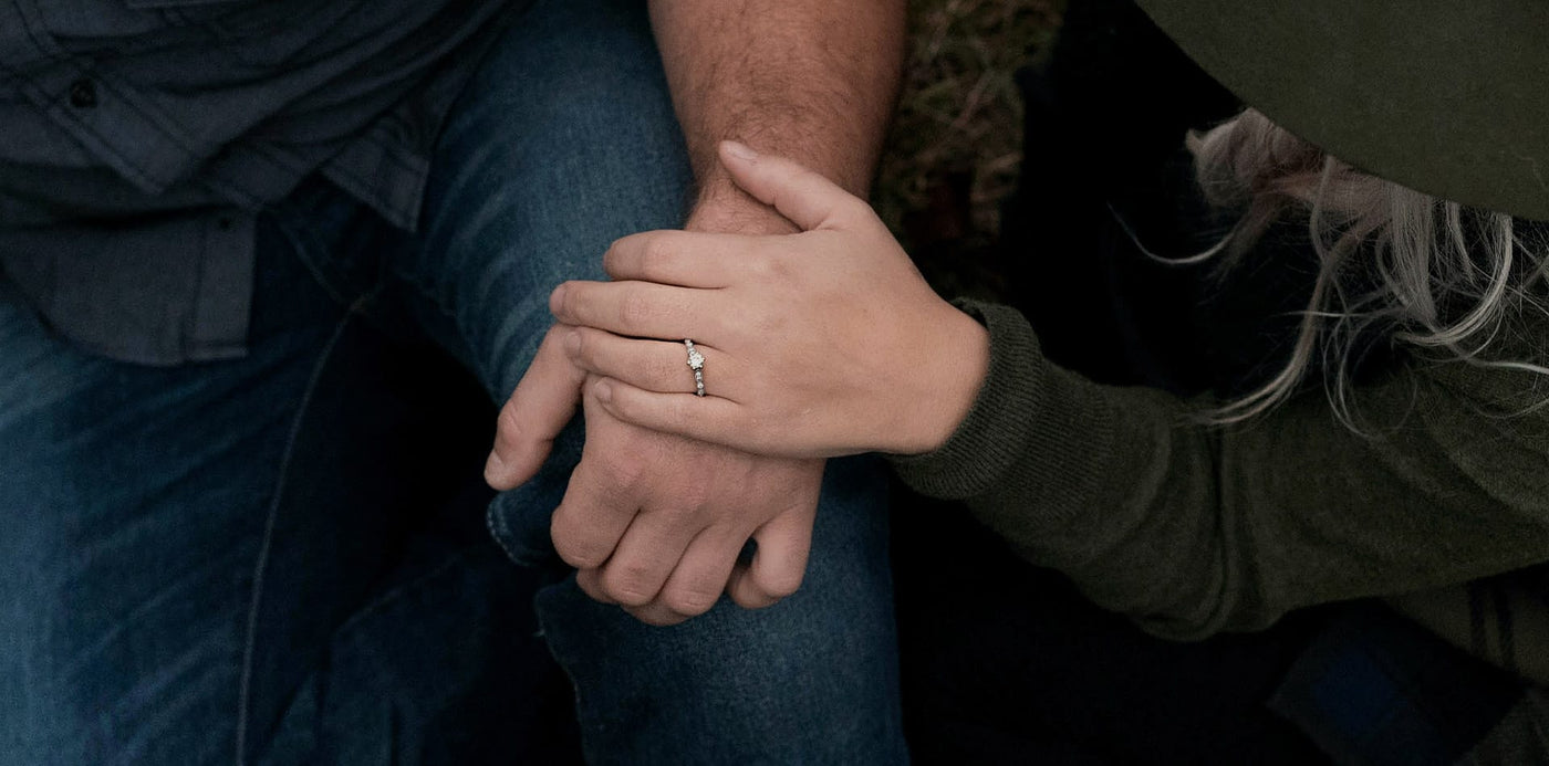 Two people holding hands, with the top hand showing off an engagement ring